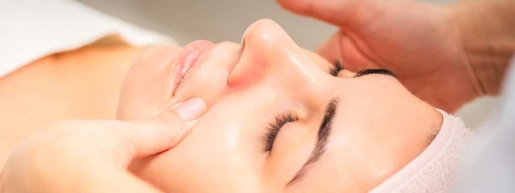 A person gently applying moisturizer to their face in a softly lit home bathroom.